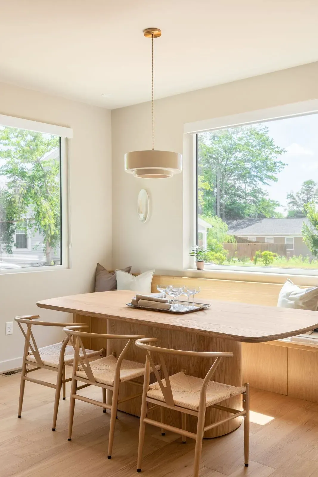 Dining room with a wood pedestal table, wishbone chairs, and banquette seating by the windows