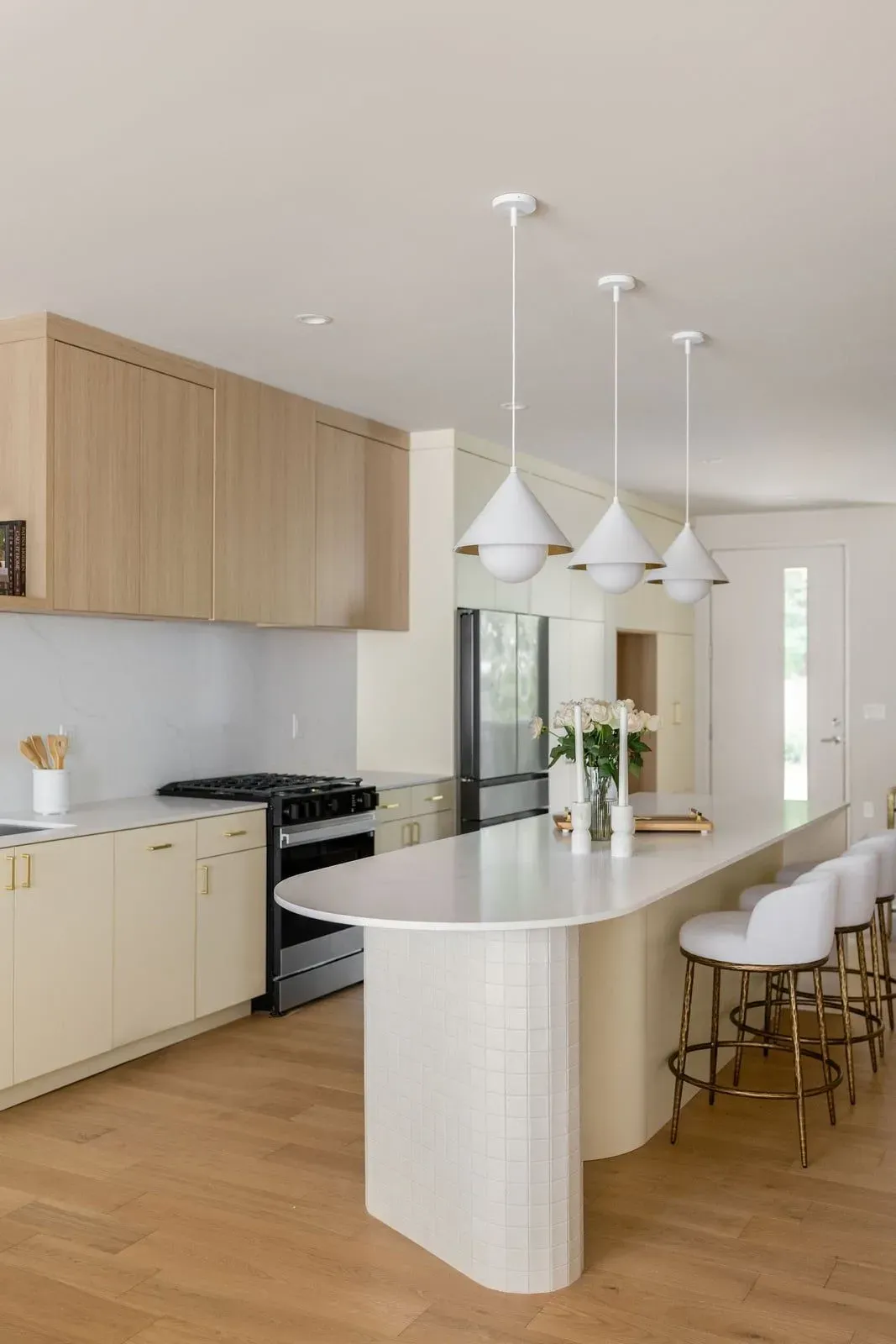 Kitchen island with a rounded white counter, cone pendant lights, and cream cabinetry
