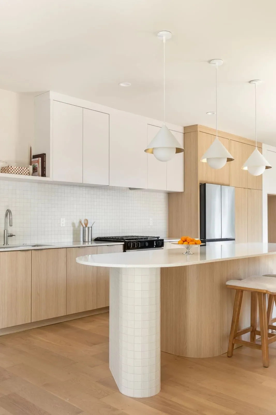 Kitchen with light wood cabinets, a tiled island pedestal, and three pendant lights