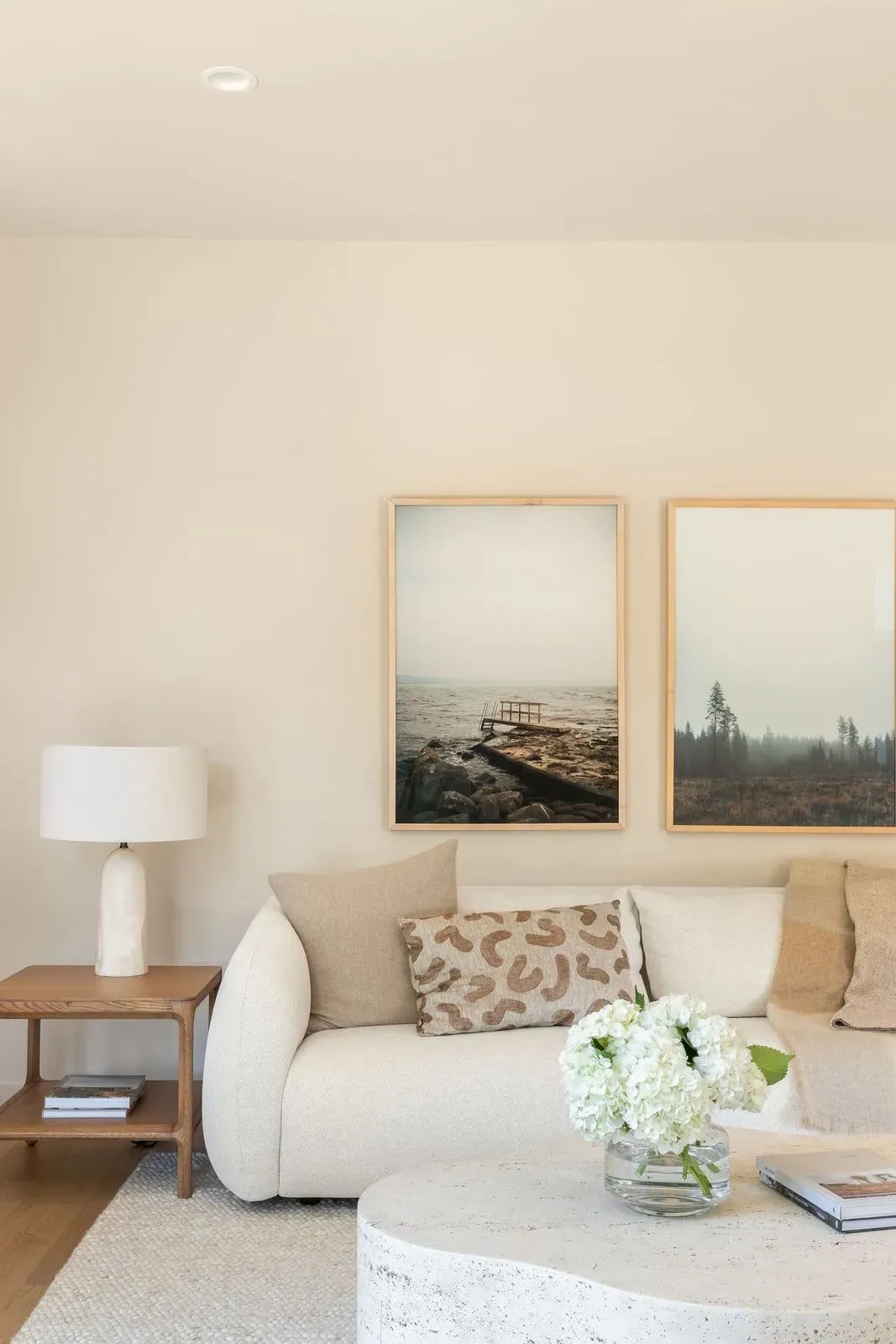 Cream sofa with landscape prints above, a stone coffee table, and a ceramic lamp